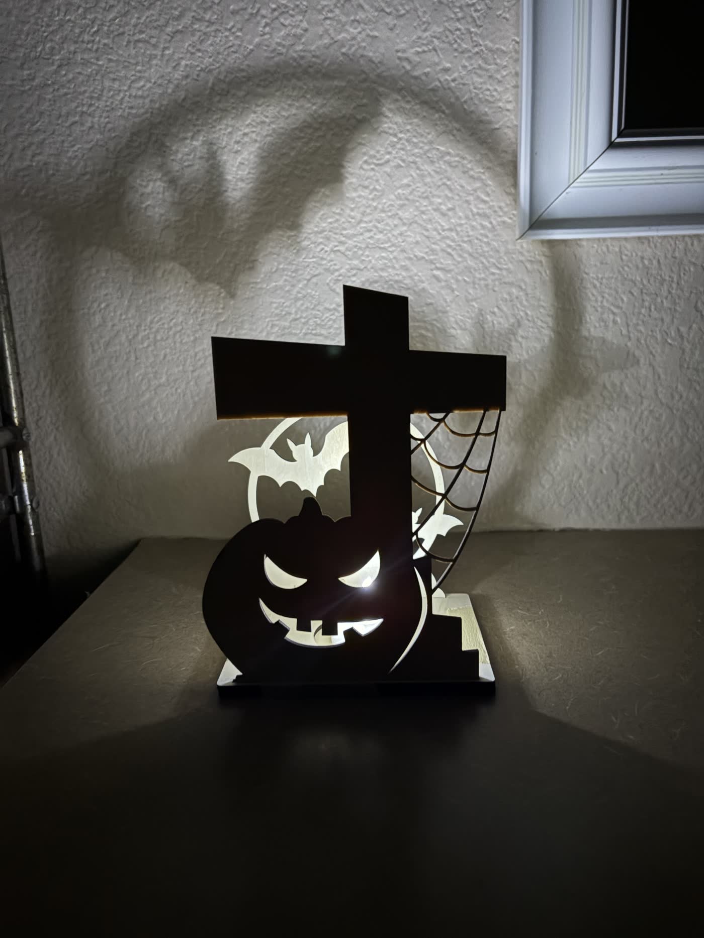 Wooden Halloween lantern with a pumpkin, cobweb, and bats casting a large bat shadow on the wall.
