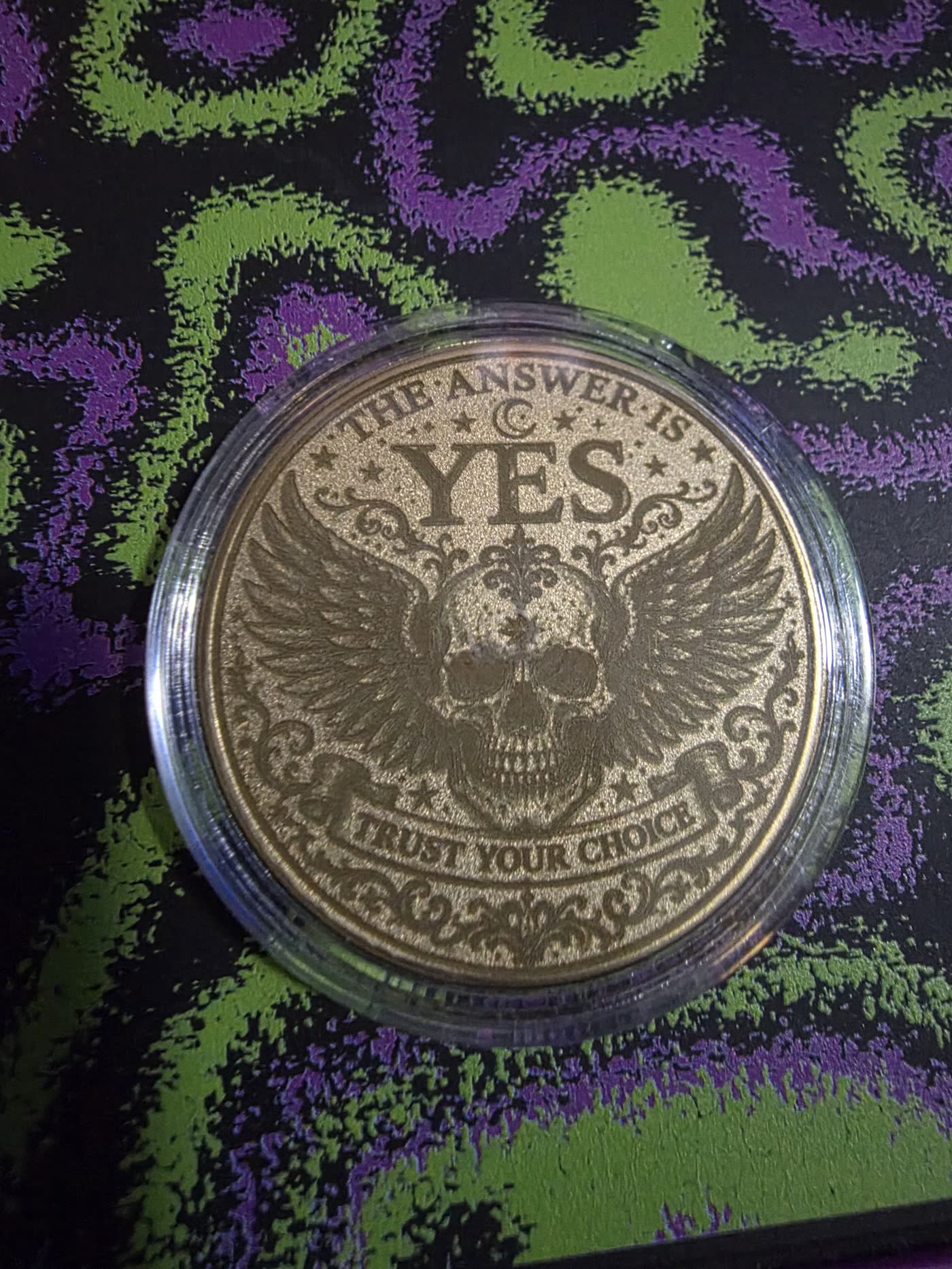 Gold metal decision coin engraved with a winged skull and the words The Answer Is Yes, Trust Your Choice.