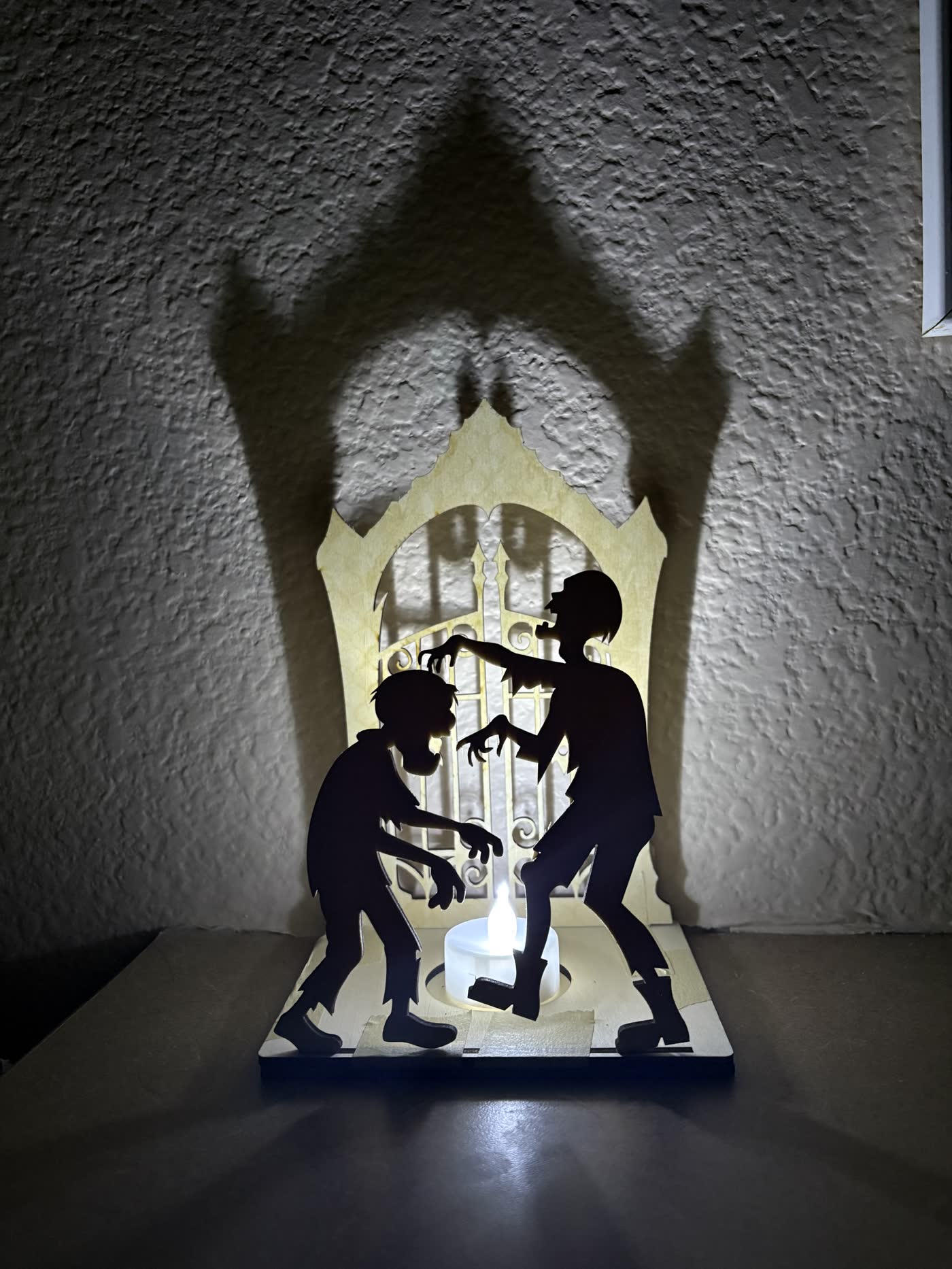 Wooden Halloween lantern with two zombie silhouettes in front of an arched gate, lit from behind.